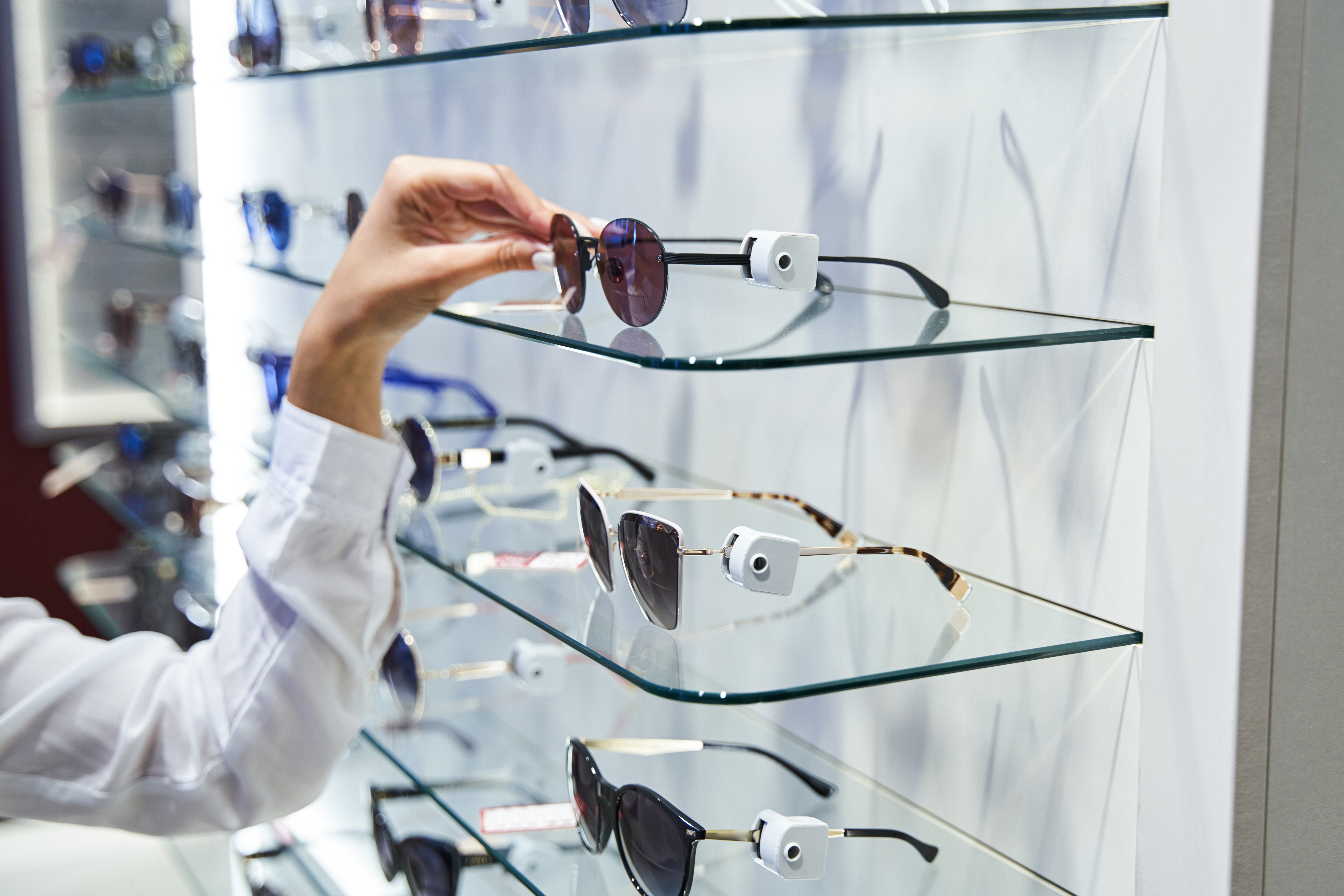 Female hand taking sunglasses from glass shelf in optical shop