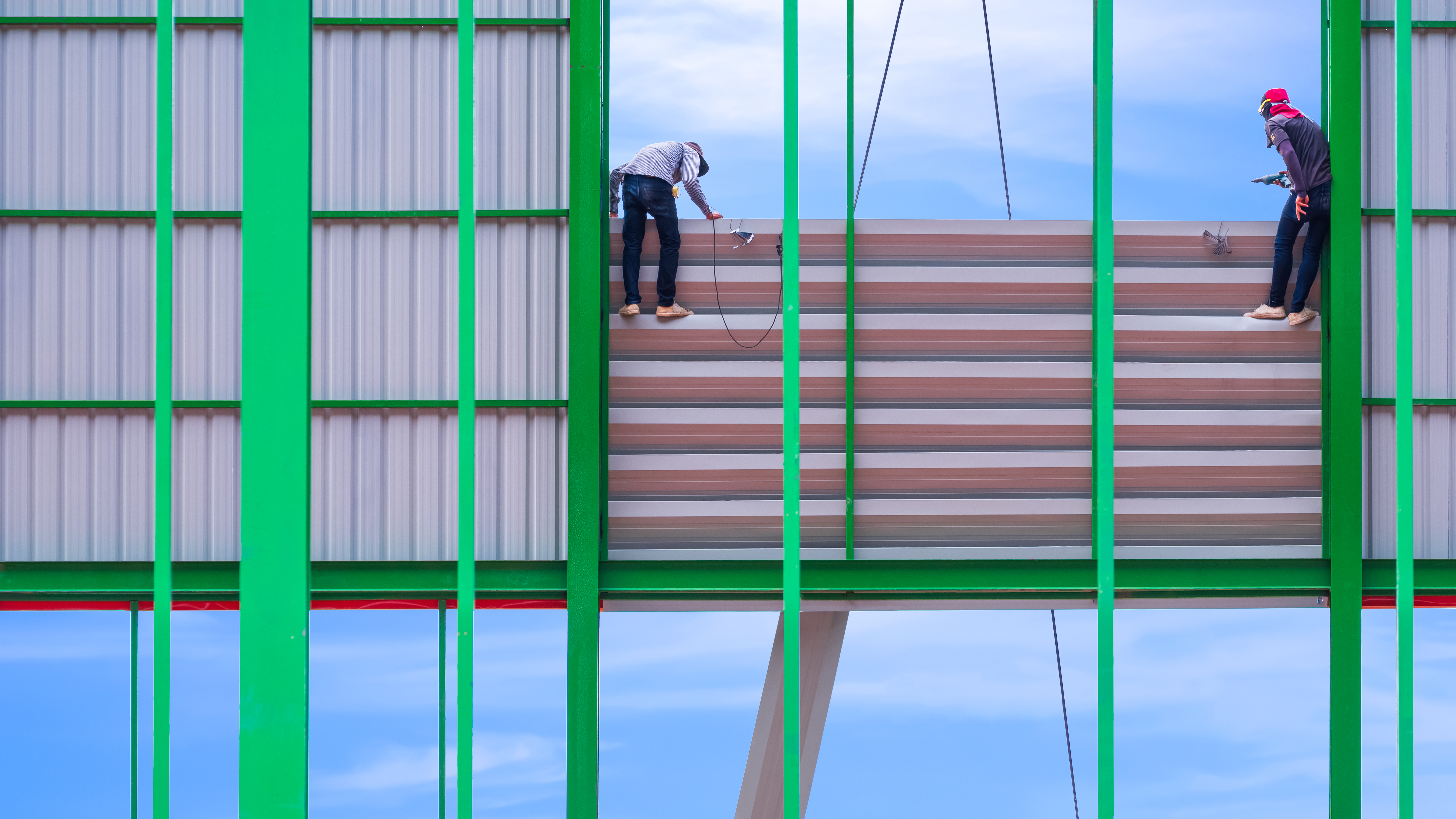 Two workers installing aluminum louver on industrial building structure in construction site